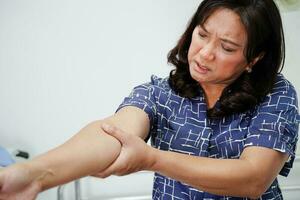 Asian senior woman wearing elastic support elbow brace for reduce pain. photo