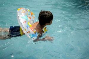 Happy Indian boy swimming in a pool, Kid wearing swimming costume along with air tube during hot summer vacations, Children boy in big swimming pool. photo