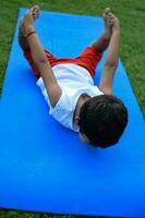 asiático inteligente niño haciendo yoga actitud en el sociedad parque exterior, para niños yoga pose. el pequeño chico haciendo yoga y meditación ejercicio. foto