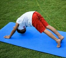 asiático inteligente niño haciendo yoga actitud en el sociedad parque exterior, para niños yoga pose. el pequeño chico haciendo yoga y meditación ejercicio. foto