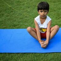 asiático inteligente niño haciendo yoga actitud en el sociedad parque exterior, para niños yoga pose. el pequeño chico haciendo yoga y meditación ejercicio. foto