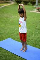 asiático inteligente niño haciendo yoga actitud en el sociedad parque exterior, para niños yoga pose. el pequeño chico haciendo yoga y meditación ejercicio. foto