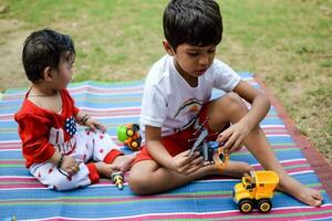 dos contento Niños en sociedad parque, contento asiático hermanos quien son sonriente felizmente juntos. hermanos jugar al aire libre en verano, mejor amigos. niñito bebé chico jugando con su contento hermano en el jardín foto