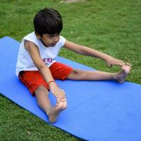 asiático inteligente niño haciendo yoga actitud en el sociedad parque exterior, para niños yoga pose. el pequeño chico haciendo yoga y meditación ejercicio. foto