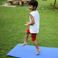 asiático inteligente niño haciendo yoga actitud en el sociedad parque exterior, para niños yoga pose. el pequeño chico haciendo yoga y meditación ejercicio. foto