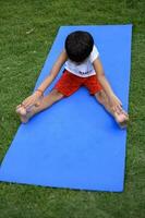 asiático inteligente niño haciendo yoga actitud en el sociedad parque exterior, para niños yoga pose. el pequeño chico haciendo yoga y meditación ejercicio. foto