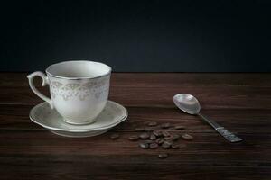 Empty coffee mug on a saucer, coffee beans on dark table boards. Beautiful silver spoon. Place for text. photo