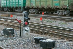 Rails with freight cars in the background and a semaphore with a glowing red light in the foreground. Selective focus on the semaphore. Background with wagons blurred. photo