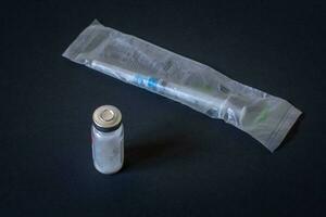 Disposable syringe in package and vial with white powder. Dark background. Horizontal. photo