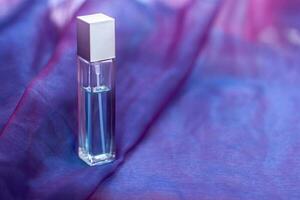 A long faceted bottle with liquid and copy space is placed on a soft cloth. An elongated glass vial with a metal cap. Blank for mock up. Shallow depth of field. Horizontal. photo