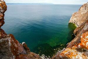 View of Lake Baikal with green transparent water from a cliff. The rock is covered with red moss. Sunny. photo