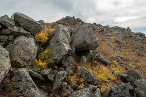 Many large rocky stones on a hillside. Rare bushes of grass between the stones. Clouds in the sky. photo