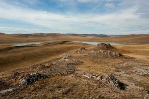 Steppe with hills and a lake. Brown grass on the ground. There are clouds in the sky. photo