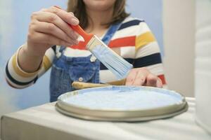 Close up of a woman's hand removing a brush with blue paint from a tray with paint photo