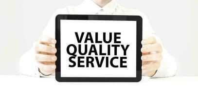 Text value quality service on tablet display in businessman hands on the white background. Business concept photo