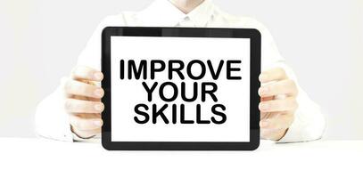 Text IMPROVE YOUR SKILLS on tablet display in businessman hands on the white background. Business concept photo