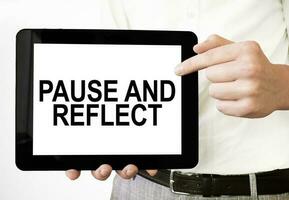 Text PAUSE AND REFLECT on tablet display in businessman hands on the white background. Business concept photo