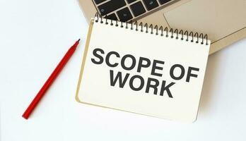 Laptop, red pen and notepad with text scope of work in the white background photo