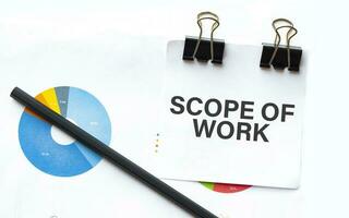 Notepad with text scope of work on business charts and pen photo