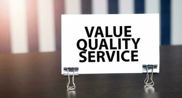 value quality service sign on paper on dark desk in sunlight. Blue and white background photo