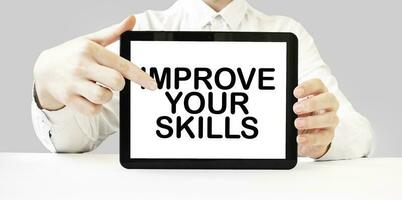 Text IMPROVE YOUR SKILLS on tablet display in businessman hands on the white background. Business concept photo