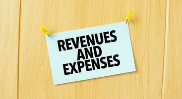 REVENUES AND EXPENSES sign written on sticky note pinned on wooden wall photo