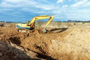 excavadora cavar las trincheras en un sitio de construcción. zanja para colocar tuberías de alcantarillado externas. sistema de drenaje de aguas residuales para un edificio de varios pisos. cavando la base del pozo foto