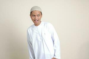 Portrait of attractive Asian muslim man in white shirt showing shocked expression and looking aside. Isolated image on gray background photo