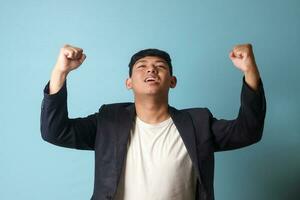 Portrait of young Asian business man in casual suit happily celebrating something good. Isolated image on blue background photo