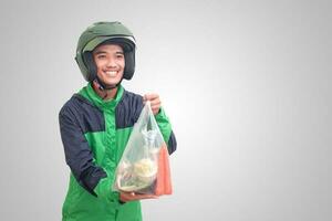 retrato de asiático en línea Taxi conductor vistiendo verde chaqueta y casco entregando el vegetales desde tradicional mercado y señalando con dedo. aislado imagen en blanco antecedentes foto