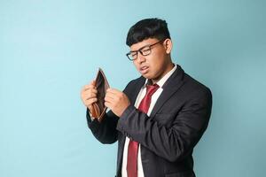 Portrait of young Asian business man in casual suit looked surprised while checking at empty leather wallet. Isolated image on blue background photo