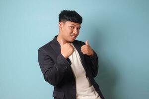 Portrait of young Asian business man in casual suit doing double thumbs up with happy expressions looking at camera. Isolated image on blue background photo