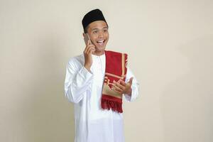 Portrait of attractive Asian muslim man in white shirt making phone call with explaining hand gesture. Isolated image on gray background photo