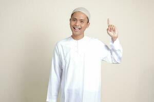 Portrait of attractive Asian muslim man in white shirt pointing up his forefinger and reminding something to do. Advertising concept. Isolated image on gray background photo