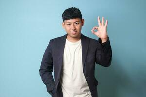 Portrait of young Asian business man in casual suit agreeing at something with happy expressions. Isolated image on blue background photo