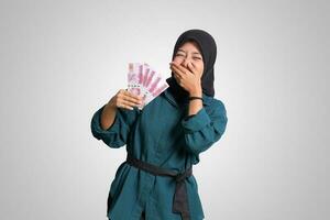 Portrait of excited Asian hijab woman in casual outfit showing one hundred thousand rupiah. Financial and savings concept. Isolated image on white background photo