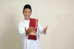 Portrait of attractive Asian muslim man in white shirt showing product and pointing with his hand and finger to the side. Isolated image on gray background photo