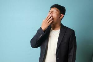 Portrait of young Asian business man in casual suit yawning in bored expressions. Isolated image on blue background photo