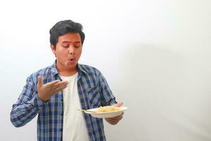 retrato de conmocionado asiático hombre en tartán camisa comiendo picante fideos y torneado su cara volverse rojo. aislado imagen en blanco antecedentes foto