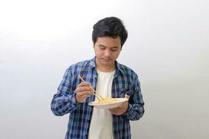 Portrait of happy Asian man in blue plaid shirt eating delicious instant noodles with chopsticks served on plate. Isolated image on white background photo