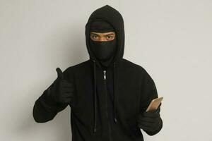 Portrait of mysterious man wearing black hoodie and mask doing hacking activity on mobile phone, hacker holding a smartphone. Isolated image on gray background photo