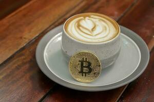 A cup of cappuccino with bitcoin on wooden table at cafe. Cryptocurrency trading concept photo