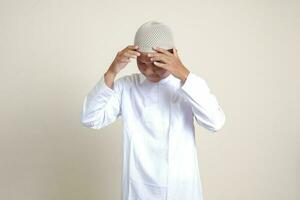 Portrait of attractive Asian muslim man in white shirt having a migraine, touching his temple. Headache disease concept. Isolated image on gray background photo