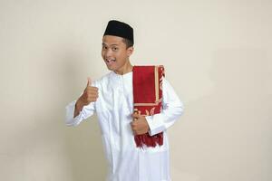 Portrait of attractive Asian muslim man in white shirt showing thumb up, good job hand gesture. Isolated image on gray background photo