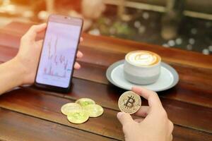 Close up of male hand holding bitcoin and mobile phone with candlestick chart on screen. Cryptocurrency trading concept photo