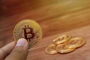 Close up of male hand holding bitcoin with a pile of coin on the wooden table background. Cryptocurrency trading concept photo