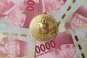 Bitcoin placing on the top of one hundred thousand rupiah bank note. Cryptocurrency trading concept photo