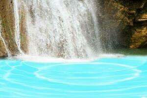 Beautiful waterfall in forestry with blue water with ripples on the surface. Blurred transparent blue colored clear calm water surface texture with splashes and bubbles. Water waves with shining. photo