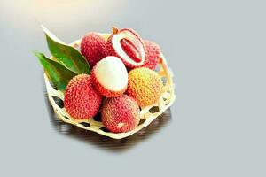 lychees in a bamboo basket. The fruit has a rough skin. They are reddish pink or bright red. seed coat Milky white that is full of water. The flesh gives a slightly sweet and sour taste. photo