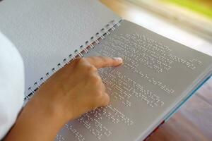 visualmente dañado persona lee con su dedos un libro escrito en braille eso es escrito para esos quien son visualmente dañado o ciego. eso es un especial código generado desde 6 6 puntos en el caja. foto